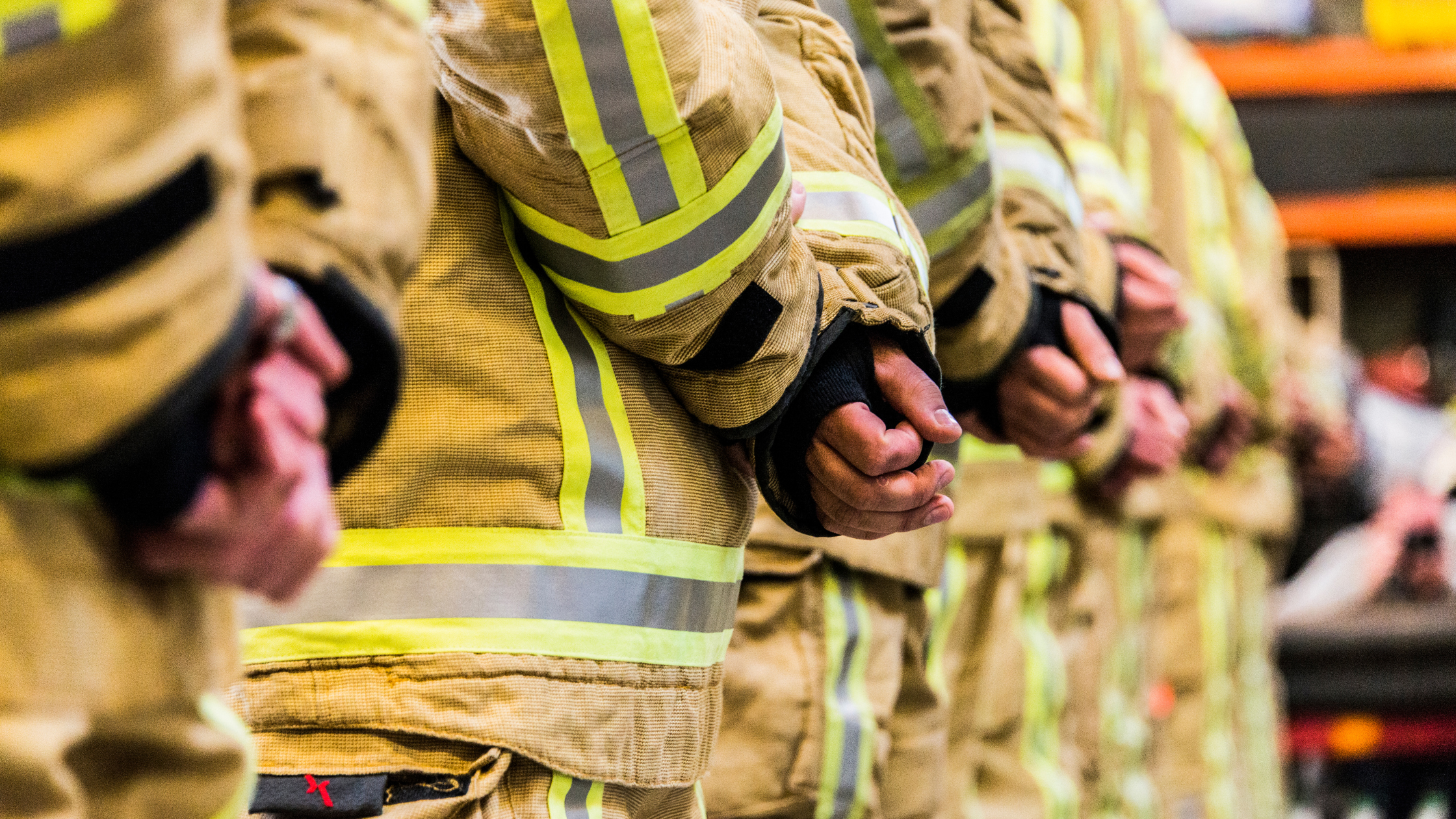Closeup of firefighters side-by-side with their hands folded at attention